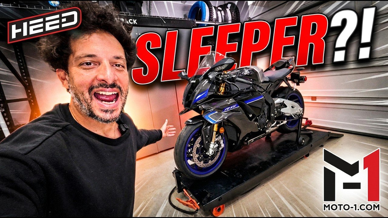 Adam Waheed grins beside a carbon fiber 2026 Yamaha YZF-R1M with blue magnesium wheels on a garage lift in Moto-1 "Sleeper?!" thumbnail art