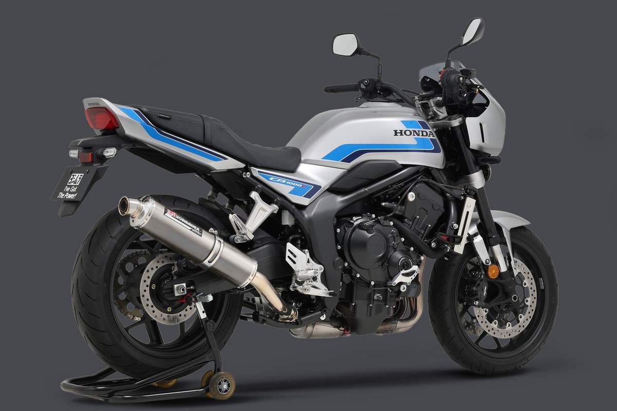 Wolf Silver Metallic 2026 Honda CB1000F with blue stripes on a rear paddock stand, fitted with a Yoshimura Japan Cyclone slip-on with titanium muffler, right-side rear three-quarter view on a gray studio backdrop